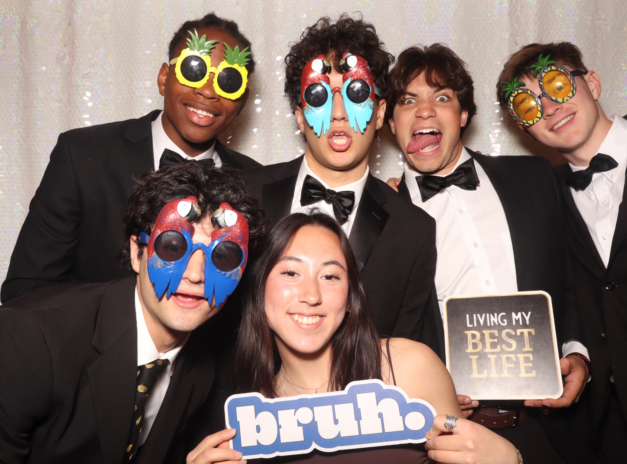 Six Harvard students in formal attire pose in a photo booth during the Johnnies with props.
