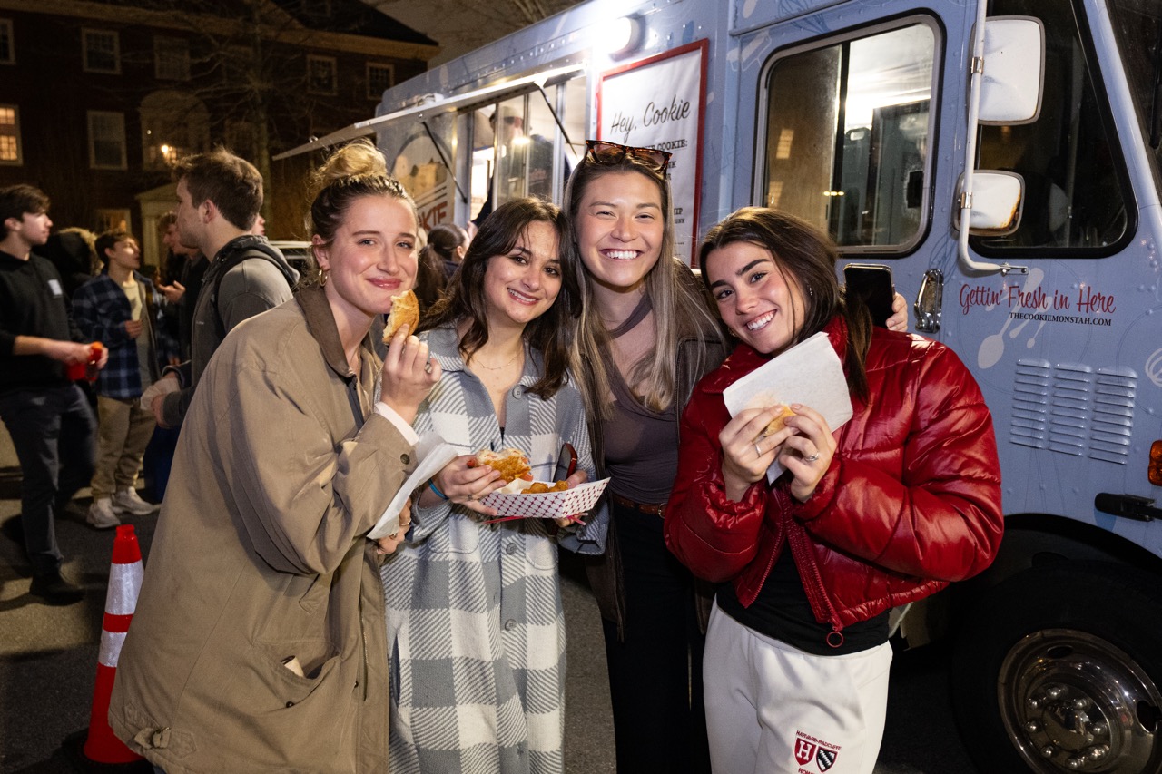 Four students hold up their food after visiting the food trucks on the MAC Quad during Housing Day Eve Programming.
