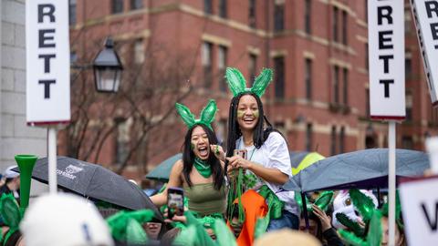 Two students on the shoulders of other students during Housing Day in the Yard with Leverett House green bunny ears on.