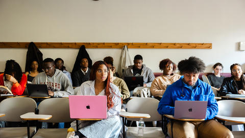 Students sit in the classroom during lecture and take notes on their laptops.