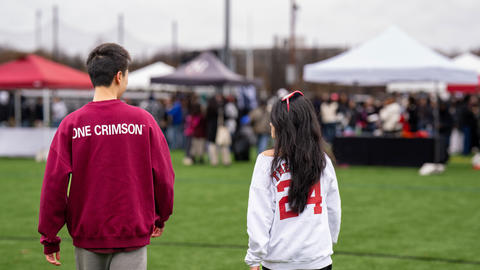 Students at the Harvard-Yale tailgate walk towards a tent with their backs to the camera talking to each other with Harvard sweatshirts.