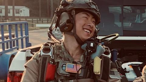 Kevin Fischetto in army fatigue and gear smiling while leaning against a truck.