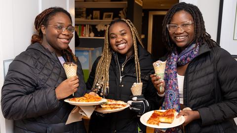 Three students pose for a photo with pizza and ice cream at the Dean of Students residence during Housing Day Eve.