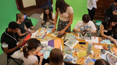 Students gather around the crafts table creating visual designs