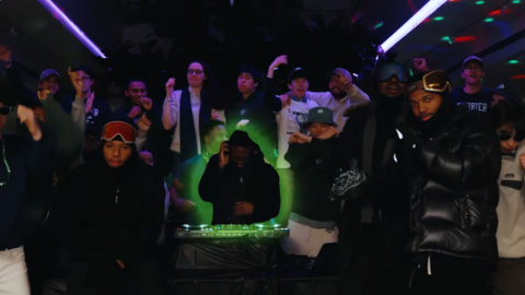 A snapshot of the Currier House Housing Day video with students gathered around at a dark party inside Currier House with one student illuminated in green.