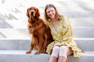 Jess Cmiel sits on Widener steps with her dog in a yellow dress smiling for the camera.