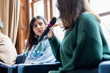 A panel speaker looks directly at their co-presenter as she shares her thoughts through a microphone during a speaker series.