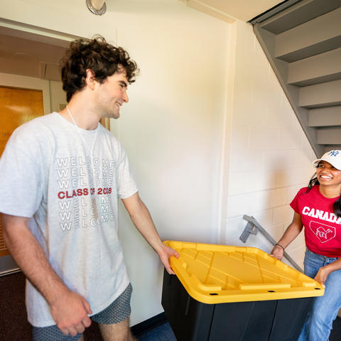 Two students move a black and yellow bin in the first-year dorms in the Yard.