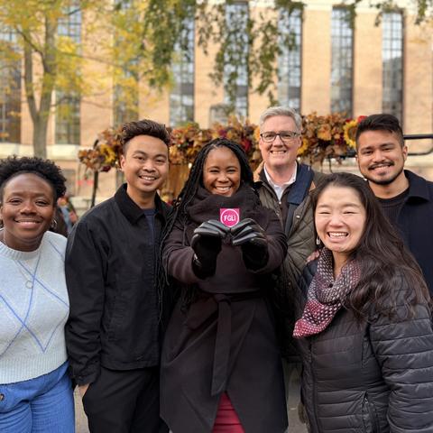 Dean of Students Office staff hold up a FGLI sticket in front of a flower truck outside of Boylston Hall.