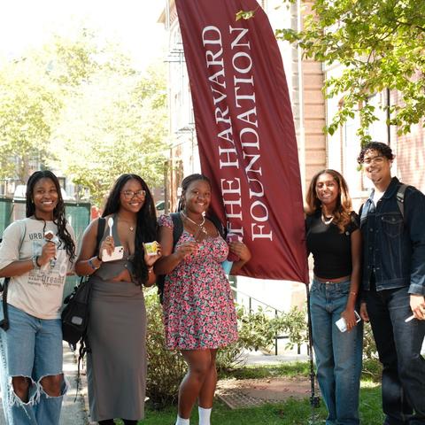 Five students pose next to the Harvard Foundation flag with ice creams in hand during a Harvard Foundation ice cream social in Harvard Yard.