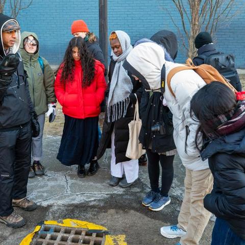 A facilitator talks to students outside in front of a grate during a sustainability program.