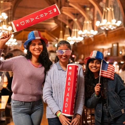 Three students in Annenberg dining hall in election night gear during the 2024 presidential elections watch party.