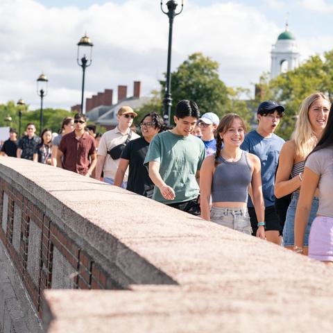 A large group of students traversing the Memorial Bridge to the Harvard Stadium