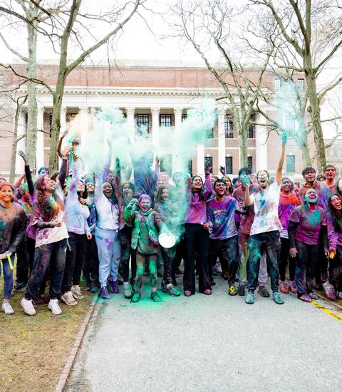 Attendees from the 2025 Holi celebration gathered in front of Widener Library after the end of the program and throw up colored powders.