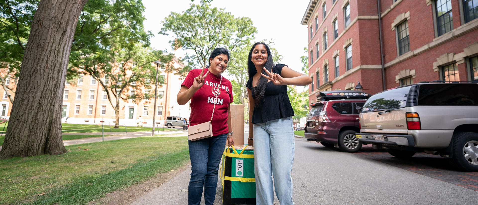 A first-year student and their mom pose for a photo on first-year move-in day in teh Yard as they pull boxes.