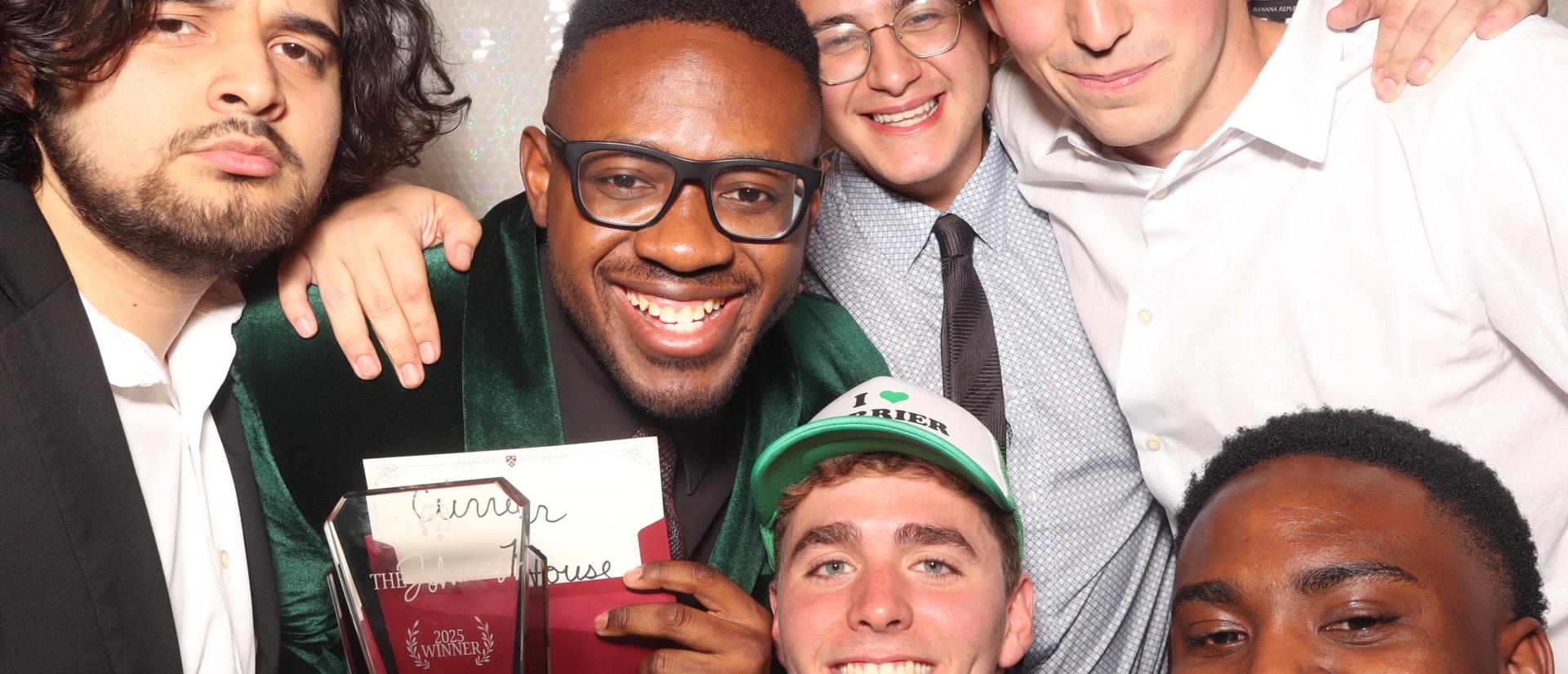 Students from Currier House pose for a photo in a photo booth with their award after winning a Johnnie.