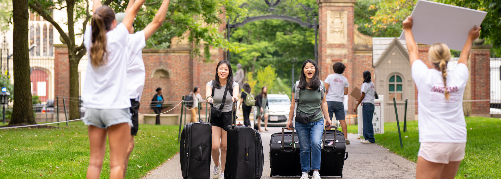 Student orientation leaders from the Crimson Key Society hold welcome signs and help welcome new students at first-year move-in in Harvard Yard.