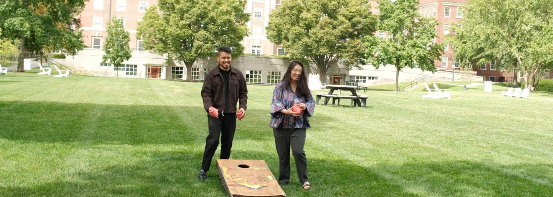 Two staff members throw corn hole bags on the quad during a sunny fall day.