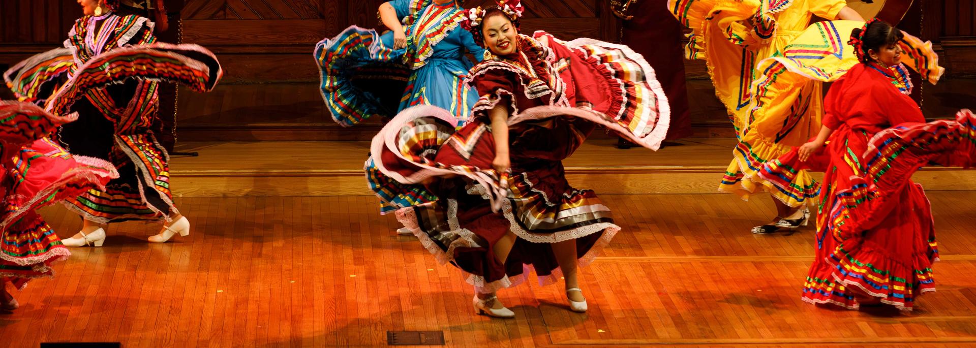 Student performers in traditional Latin American garb dance on stage in Sanders Theater during the Cultural Rhythms program.