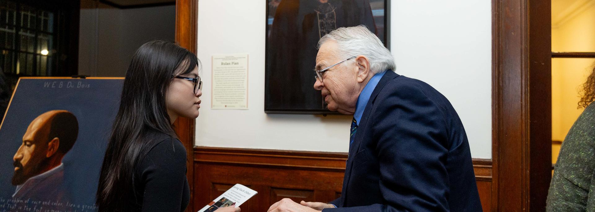 Student speaks with artist in front of portraiture of Rulan Pian.