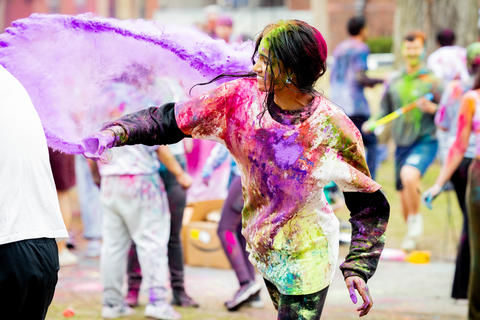 A student covered in different colors hurls a hand full of powders at a peer during the 2025 Holi celebration in the Yard.