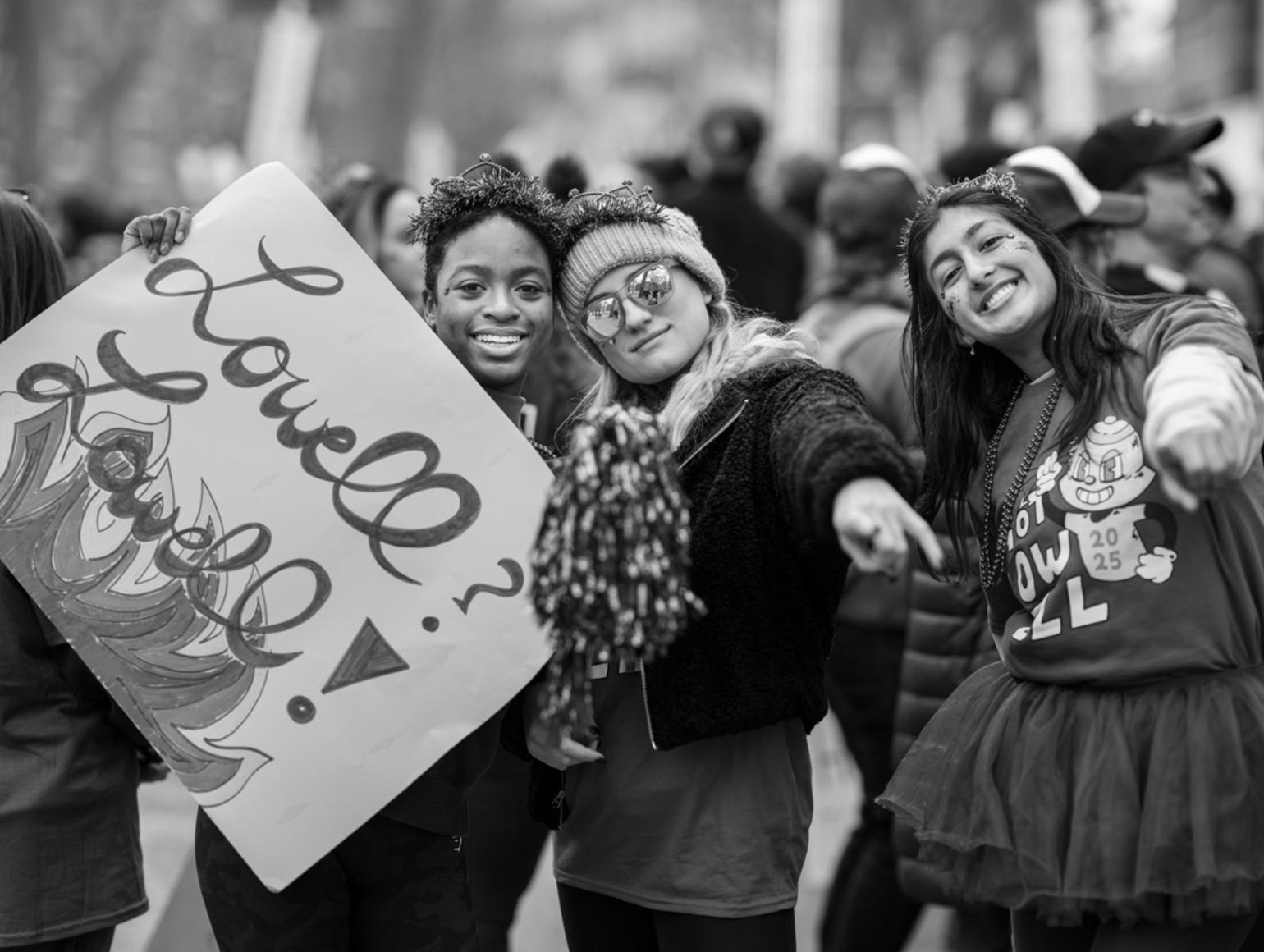 Black and white photo with three Lowell House students posing with their sign and Lowell House SWAG on Housing Day during the Yard storm.