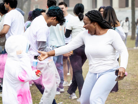Dean Alta Mauro at the Holi Celebration in Harvard Yard spraying an attendee with pink powder.