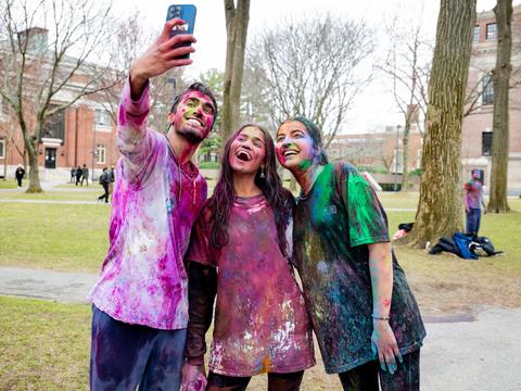 Three students pose for a selfie in Haravrd Yard after the 2025 Holi celebration covered in colors.