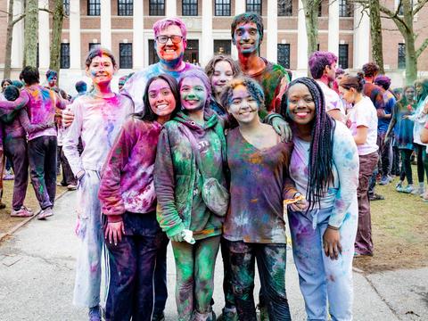 Dean Tom Dunne and Dean Alta Mauro pose with their families in front of Widener Library covered in colors during the 2025 Holi celebration.