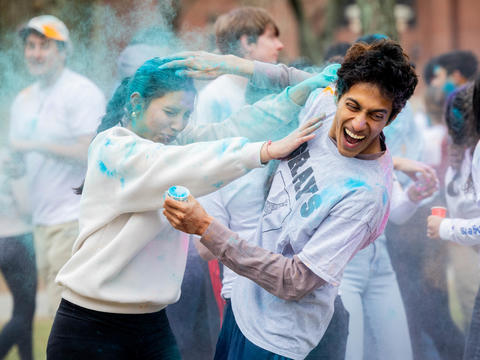 Two students smear blue-colored powders on their head and clothing during the 2025 Holi celebration in Harvard Yard.