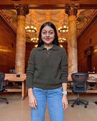 Gabriella Dumancela smiles while standing in a grand wood-paneled room with marble columns and ornate ceiling lights