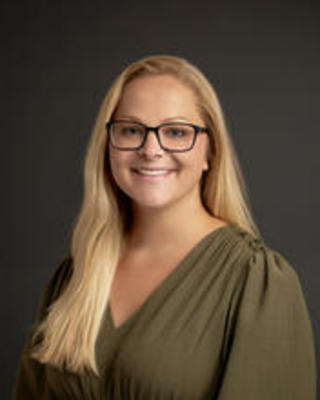 White woman in green shirt with blond hair and glasses smiling at camera