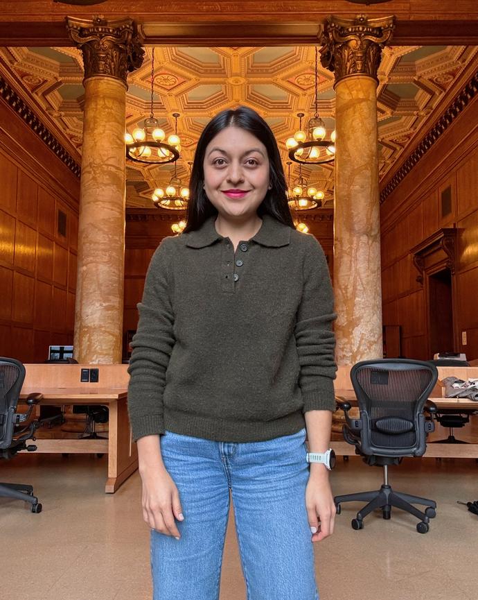 Gabriella Dumancela smiles while standing in a grand wood-paneled room with marble columns and ornate ceiling lights